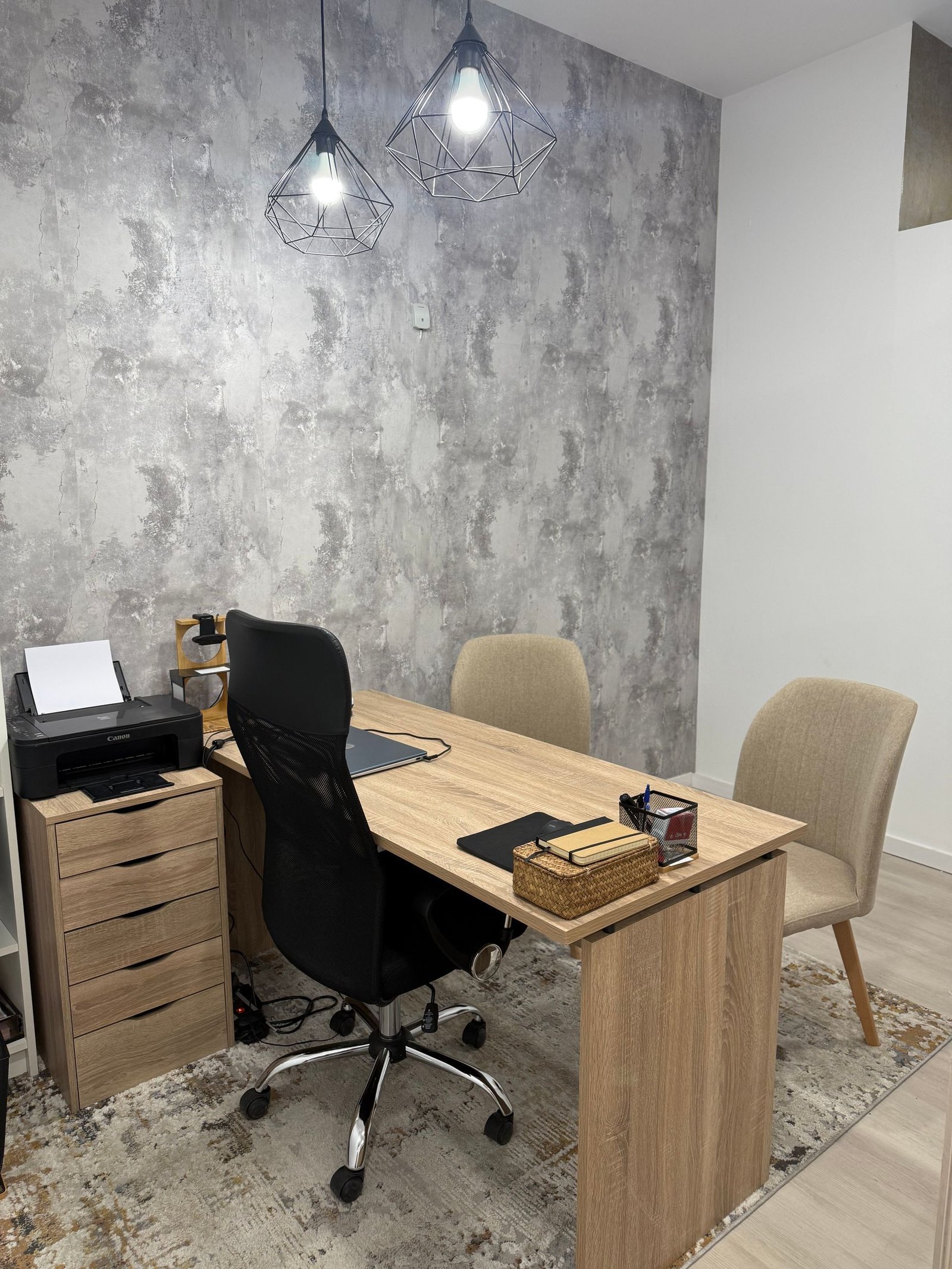 Oficina con escritorio, sillas, pared texturizada, lámparas colgantes e impresora.